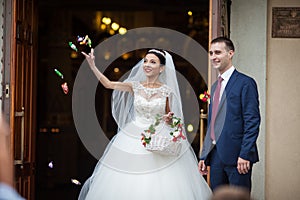 Happy newlywed romantic couple coming out of church after wedding ceremony with a candy basket