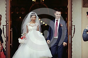 Happy newlywed romantic couple coming out of church after wedding ceremony with a candy basket