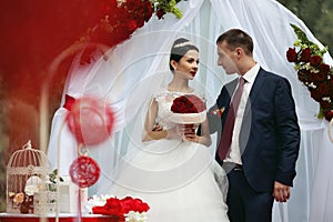 Happy newlywed romantic couple at wedding aisle with red decorations and flowers