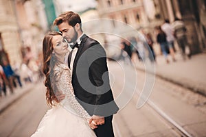 Happy newlyweds couple on a walk in old European town street, gorgeous bride in white wedding dress together with handsome groom