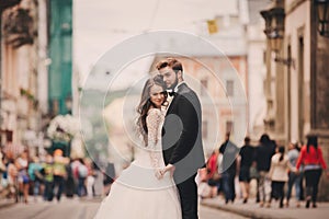 Happy newlyweds couple on a walk in old European town street, gorgeous bride in white wedding dress together with handsome groom