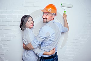 Happy newlyweds family handsome man in the construction helmet hardhat and charming woman together painting white brick