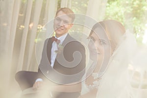 Happy newlyweds holding hands and sitting on beige sofa in park