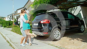 Happy newlyweds hug after packing all of their luggage in the back of their car.