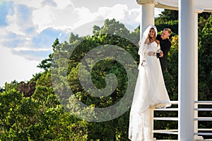 Happy newlyweds stand on the metal fence of the gazebo and look into the distance