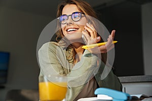 Happy nice student woman talking on mobile phone while doing homework