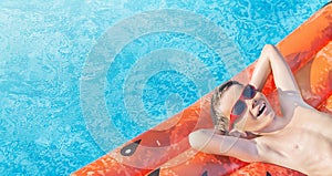 Happy nine years old caucasian child boy in red sunglasses having fun on inflatable ring air mattress in swimming pool.