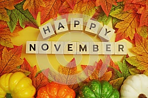 Happy November alphabet letter with pumpkin and maple leaves decoration on yellow background