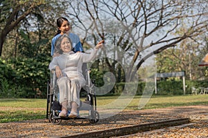 Happy nurse and elderly woman sitting in wheelchair enjoying outdoor. Beautiful nurse with senior woman in wheelchair at