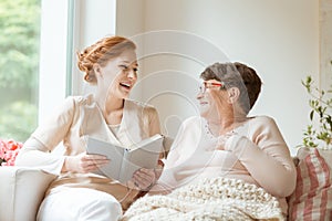 Happy nurse reading a funny book to her elderly patient in a private nursing home