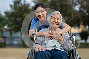 happy nurse take care and embracing with senior woman patient in wheelchair at park