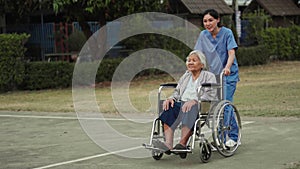 happy nurse take care and pushing senior woman in wheelchair at park, friendly caregiver