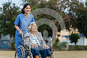 happy nurse take care and pushing senior woman in wheelchair at park, friendly caregiver