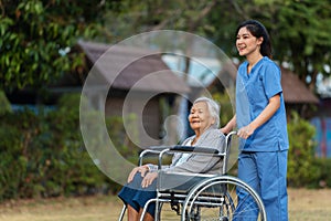 happy nurse take care and pushing senior woman in wheelchair at park, friendly caregiver
