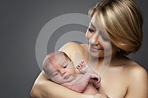 Happy nursing mother with a newborn baby in her arms. Love and tenderness. Gray background. Space for text