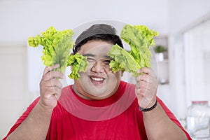 Happy obese man holds fresh lettuce in kitchen
