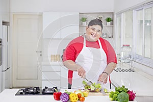 Happy obese man mixing fresh salad in the kitchen