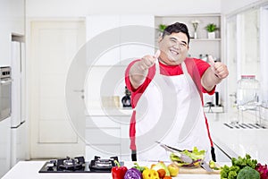 Happy obese man showing thumbs up in kitchen