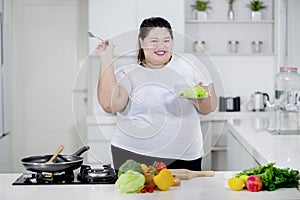 Happy obese woman eating salad in the kitchen