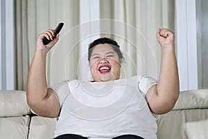 Happy obese woman watching television at home