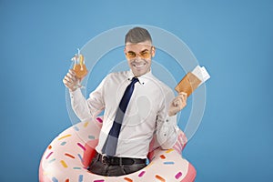 Happy office worker with passport, tickets, inflatable ring and cocktail dreaming of summer vacation, blue background