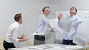 Happy office workers are excited in workplace having fun throwing papers documents enjoying success