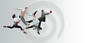 Happy office workers in face masks jumping and dancing in casual clothes or suit isolated on studio background. Creative
