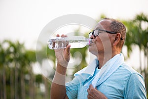 A happy old asian man is drinking water at park with sunlight. Healthcare and senior sports concept