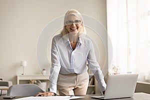 Happy old business woman in elegant clothes standing at workplace