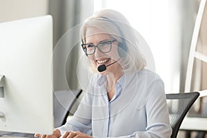 Happy old businesswoman in headset making call looking at computer