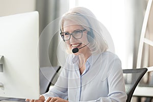 Happy old businesswoman in headset making call looking at computer photo