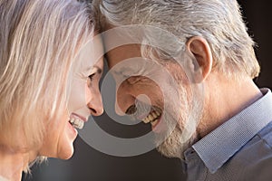 Happy old couple bonding touching foreheads laughing, closeup side view photo