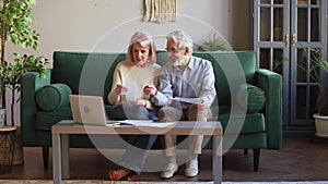 Happy old couple calculating domestic bills at home with laptop