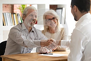 Happy old couple clients make financial deal handshake meeting lawyer