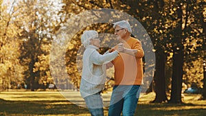 Happy old couple dancing in park. Senior man flirting with elderly woman. Romance at old age autumn day