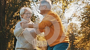 Happy old couple dancing in park. Senior man flirting with elderly woman. Romance at old age autumn day