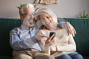 Happy old couple holding smartphone looking at cellphone screen laughing