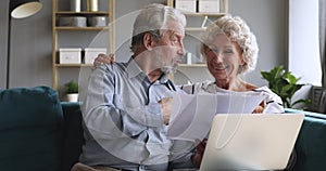 Happy old couple talking checking papers holding bills and laptop