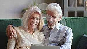 Happy old couple talking laughing doing internet shopping using laptop