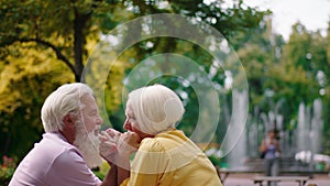 Happy old couple very romantic in the middle of park at cafe hugging hands and looking at each other and discussing