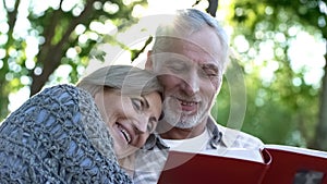 Happy old couple watching photobook and smiling, pleasant youth memories, fun