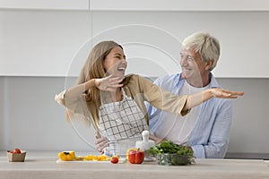 Happy old father hugging pretty young adult daughter in kitchen