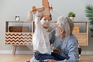 Happy old grandfather and cute grandson playing with wooden plane