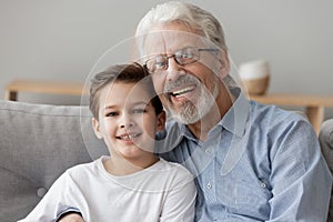 Happy old grandfather embracing little child grandson looking at camera