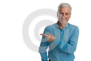 Happy old guy in denim shirt smiling while pointing finger to side