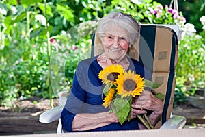 Happy Old Lady Sitting on Chair Holding Sunflowers