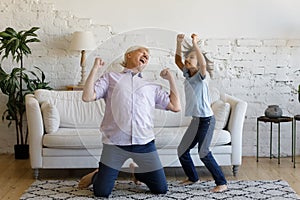 Happy old man dancing with preteen grandson at home.