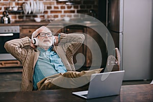 Happy old man in headphones using laptop with feet