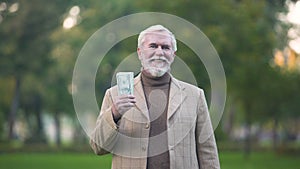 Happy old man holding dollar bills in hand, retirement savings, pension fund