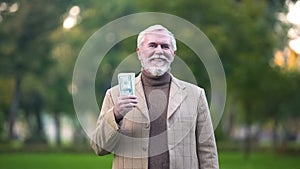 Happy old man holding dollar bills in hand, retirement savings, pension fund